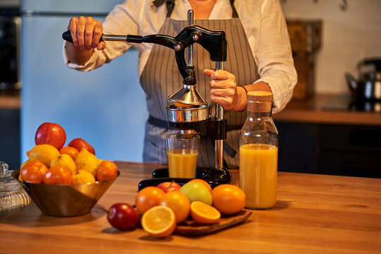 Person making orange juice using a manual juicer with fruits and a bottle on a wooden table.